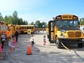 Students safety board a school bus for their first ride while proud family members look on.