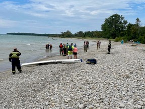 People watch as two firefighters bring ashore an exhausted man at Lorne Beach, in the municipality of Kincardine, on Aug. 1, 2022. The number of Lake Huron rescue calls has spiked this year in Kincardine. (Kincardine Fire and Emergency Services Chief Brad Lemaich photo)