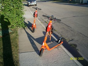 Scooters sit on the sidewalk unnattended.