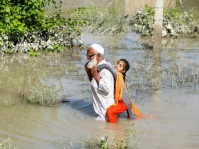 Un homme patauge dans les eaux de crue et porte sa petite-fille sur son dos après la pluie et les inondations pendant la saison de la mousson à Charsadda, au Pakistan.  Fayez Aziz/Reuters