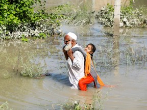 Un homme patauge dans les eaux de crue et porte sa petite-fille sur son dos après la pluie et les inondations pendant la saison de la mousson à Charsadda, au Pakistan. Fayez Aziz/Reuters