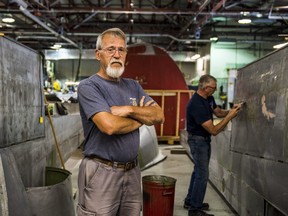 National Air Force Museum of Canada Restoration Technician Mike Joly stands between two "flaps" of the museum's Lancaster KB 882 aircraft as volunteer Dave Shepard scrapes paint and rust from the metal behind him on Thursday. ALEX FILIPE