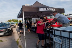 St. Marys firefighter Jeff Sass passes food to colleague Chris Primeau during a charity drive-thru the department hosted Saturday. Volunteer firefighters, in partnership with Joe’s Diner and Broken Rail Brewing, handed out $25 pork chop dinners, raising money to support various causes. Chris MontaniniStratford Beacon Herald