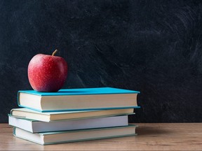 Apple and a stack of books on desk with blackboard in background