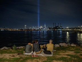 TOPSHOT - People sit before the east river and the 'Tribute in Light' installation amid the Manhattan city skyline commemorating the 9/11 terrorist attacks, in New York on September 10, 2022. (Photo by Ed JONES / AFP) (Photo by ED JONES/AFP via Getty Images)