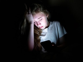 An upset girl sitting in the dark while using her smartphone. The light from the screen is illuminating her face.