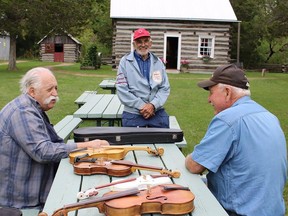 Don Dulmage of Ameliasburgh, left, displayed a sampling of violins of various sizes and styles he has made over the years. The white, small sized one was made from a packing crate, he explained. Here he chats with fellow old timers Ron Hubbs, right and Ross Chase, centre, at the Ameliasburgh Museum on Sunday. JACK EVANS PHOTO