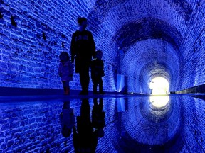 Hilary Hough, of Brockville, her daughter Ellie Chisamore, left, and son Atlas Chisamore are silhouetted by the Royal blue light of the Brockville Railway Tunnel on Monday morning. The city lit the tunnel in Royal blue to mark the funeral of Queen Elizabeth II. (RONALD ZAJAC/The Recorder and Times)