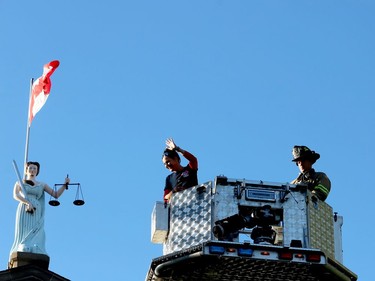 Cst. Sarah Bamford, of the Barrie Police Service, waves to Run to Remember participants from a firefighters' aerial bucket over the Court House Green, with Sally Grant in the background, accompanied by Brockville firefighter Matt Hulton. (RONALD ZAJAC/The Recorder and Times)