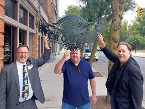 Crowfest co-chairs, Mayor Darrin Canniff, left, and Andrew Thiel, middle, are joined by John Fairley, vice-president of college communications and community relations with St. Clair College, a major sponsor, in hoisting a metal Crowfest sign on Wednesday in downtown Chatham. (Ellwood Shreve/Chatham Daily News)