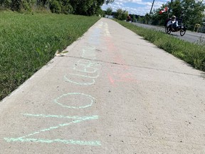 A cyclist passes sidewalk graffiti opposing the proposed redevelopment of the former Davis Tannery site in Kingston on Thursday.