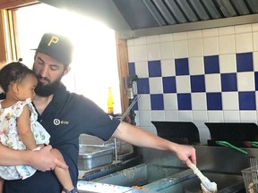 Lake Huron Fish and Chips owner Matthew Garniss holds daughter Sohla as he deep-fries whitefish for his customers.