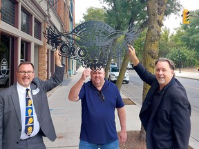 Crowfest co-chairs, Mayor Darrin Canniff (left), and Andrew Thiel, middle, are joined by John Fairley, vice-president of college communications and community relations with St. Clair College, a major sponsor, in hoisting a metal Crowfest sign in downtown Chatham. Ellwood Shreve/Postmedia