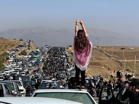 This image posted on Twitter reportedly on Oct. 26, 2022 shows an unveiled woman standing on top of a vehicle as thousands make their way towards Aichi cemetery in Saqez, Mahsa Amini's home town in the western Iranian province of Kurdistan, to mark 40 days since her death.