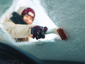Woman cleans windshield with ice scraper