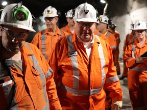 Premier Doug Ford and a group of others walk through a mine passage dressed in orange mining coveralls and white safety helmets