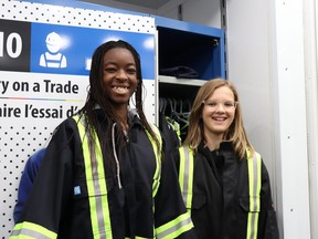 Grade 7 Ecole St.-Pierre students Divine Zahuui (left) and Sophie Memburg try on coveralls at the “Try on a Trade” station on the Skills Ontario Trade and Tech Truck during the “By Girls, For Girls” conference.