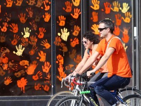 Two people ride bicycles past a window with numerous orange hand prints on it, in Winnipeg. Chris Procaylo, Friday September 30. 2022 Winnipeg Sun