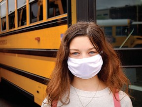 A student wears a facemask in front of a school bus. In shared indoor settings, a well-fitted mask offers real protection.