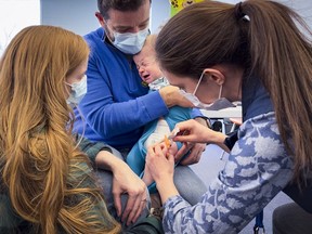 Six-month-old Elijah is comforted by his parents, Victoria and Bryan Ernst, as he receives a COVID-19 vaccine from an Ottawa Public Health nurse at a vaccination clinic on Wednesday, Nov. 23, 2022.