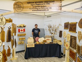 Jess Pedersen poses in his booth during a holiday market at the Frank Wills Community Hall in Cochrane on Saturday, Nov. 12, 2022. Pedersen creates various pieces by applying laser cutting and burning to wood.