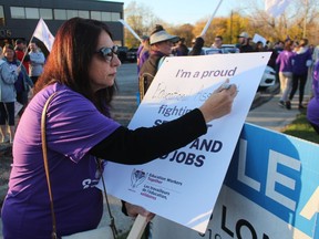 Educational assistant Afsaneh Yazdani prepares a sign while joining a rally by the Canadian Union of Public Employees and supporters Tuesday evening outside the Point Edward office of Sarnia-Lambton MPP Bob Bailey.