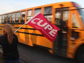 Jennifer Barnett, a staff representative with CUPE, waves the flag Friday morning at a picket line outside of Sarnia-Lambton MPP Bob Bailey's constituency office in Point Edward as a school bus passes.