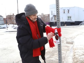 Chris Breit ties a scarf around a metal post in downtown Sudbury on Monday for the Red Scarf campaign, which is part of a number initiatives planned for Reseau ACCESS Network's HIV Awareness Week.