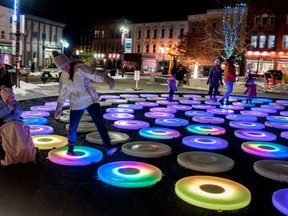 Pam Davidson gets smiles from Linda Huston and her daughter, Livy, as she skips across The Pool, an interactive light display in Stratford’s Market Square. The display, designed by artist Jen Lewin, was part last year's Lights on Stratford festival.