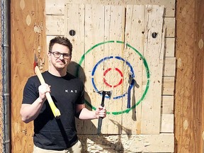 Kingston Axe Throwing staff judge Konrad Davy stands next to a target with a few types of throwing axes.
