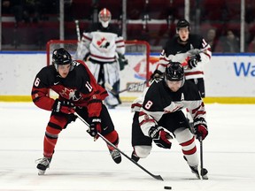 Roberts Lefevrs/Hockey Canada Images, Kanādas austrumu spēlētājs Semjuels Asinivejs pa kreisi un Kanādas Rietumu spēlētājs Briks Makkinlijs dzenas pēc ripas World Jr. Challenge laikā.  Pirmdien, 2022. gada 12. decembrī, Kornvolas pilsētvides kompleksā A. Kanādas rietumi šajā spēlē uzvarēja ar 6:3.