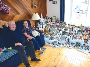 Photo by KEVIN McSHEFFREY
Garry and Julianne Romain sit by their Christmas village in the living room. They have had the village for more than 20 years. She started it with just six pieces, and it has grown into a city they call Romainville.