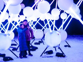 Zoie Wong dan Tim Lee, pengunjung dari Toronto, bermandikan cahaya saat berswafoto pada bulan Desember di Affinity, patung cahaya interaktif Australia di Pulau Tom Patterson Stratford sebagai bagian dari festival Lights On Stratford tahun ini.  Chris Montanini/The Beacon Herald