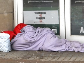 A person attempts to keep warm while resting in front of the Sudbury Community Arena on Dec. 6.