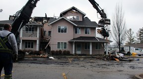 Scott Barr, hired by a property restoration company to put up fencing around Fairwinds Lodge retirement home, watches Tuesday as a heavy equipment operator removes burnt sections of the home, which was heavily damaged by a fire overnight Monday.  (Terry Bridge/Sarnia Observer)