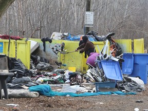 A couple of people load garbage bins at the Integrated Care Hub encampment on Montreal Street in Kingston on Friday, Jan. 6, 2023. Remaining residents of the encampment were advised that by Wednesday, Jan. 11, the encampment would be closed and any items remaining would be removed.