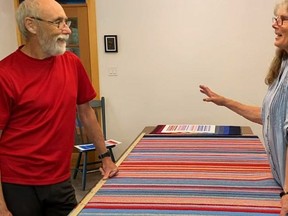 Ann Schneider dan John Anderson dengan permadani garis penghangat iklim yang ia buat dalam sebuah adegan dari film pendek Garis-garis Pemanasan: Menenun Cuaca.