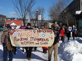 Participants marching down the sidewalk, holding a banner that reads "Remembering and Honouring Missing Murdered Indigenous Women and Girls"