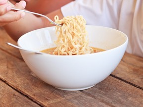 Child eating instant noodles in white bowl on wooden table. table,Focused on instant noodle.