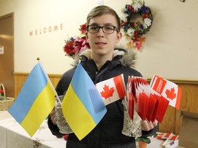 Taras Kulmatycky, 14, a member of St. John the Baptist Ukrainian Catholic Church, distributes flags on Friday, Feb.  24 at a candlelit vigil that marked the first anniversary of the war in Ukraine and 365 Days of Resistance.  MICHAEL RUBY