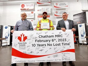 Rene Lapointe, left, manager of the Coca-Cola Bottling Ltd. plant in Chatham, Cesar Torres, co-chair of the facility's joint health and safety committee, and Bill Pickering, right, senior manager of equipment operations, are seen with a banner, on Wednesday that recognizes 10 consecutive years of no loss time accidents at the facility. There is a tradition of hanging banners, signed by employees, for each year a perfect safety record is achieved in the plant. (Ellwood Shreve/Chatham Daily News)