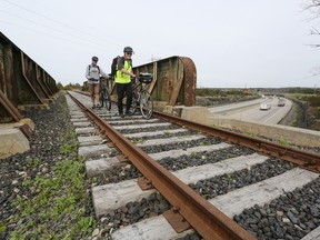 Mike Sewell and Jim Peets walk their bikes over a retired railway bridge that crosses Highway 401 in Napanee on Friday, April 29, 2023. The bridge is part of a disused stretch of CN Railway line owned by the Town of Greater Napanee. Some residents want to see the line converted to a trail for recreational use, but the town decided to surplus the property.