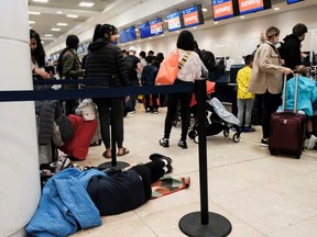 A passenger sleep as other passengers from Sunwing airlines line up for check-in at Cancun International Airport after many flights to Canada have been cancelled because of the severe winter weather conditions in various parts of the country in Cancun, Mexico, Dec. 27, 2022.
