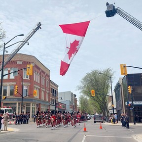 A military parade by members of the Essex and Kent Scottish Regiment passes under a large Canadian flag erected by the Chatham-Kent Fire and Emergency Services at the intersection of King Street and Fifth Street in Chatham on Sunday.  Ellwood Shreve/Chatham Daily News