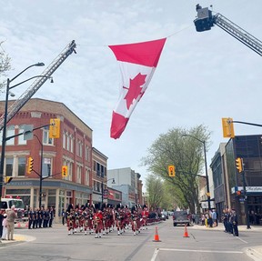 A military parade by member of the Essex and Kent Scottish Regiment passes under a large Canadian flag erected by the Chatham-Kent Fire and Emergency Services at the intersection of King Street and Fifth Street in downtown Chatham on Sunday. PHOTO Ellwood Shreve/Chatham Daily News
