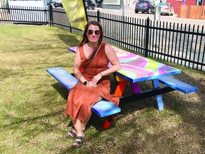 Leduc Arts Foundry President Breanne Debski hangs out on the picnic table at the Light House Cowork, which was painted at the 2022 Leduc Art Walk. This year, 10 artists will be painting tables at the 2023 Art Walk. (Dillon Giancola)