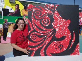 Métis artist Treasure Cooper with her artwork, "Silent Scream" at Kiyam Community Park on May 5, 2023. People at Red Dress Day events were invited to mark the canvas with red paint on their hands. The black lines were covered by tape. The painting shows a woman screaming in pain and anguish while her body is not visible. Cooper said this represents the erasure and invisibility that has surrounded the crisis of missing and murdered Indigenous women, girls and two-spirit people (MMIWG2S). The painting was donated to the Athabasca Tribal Council. Vincent McDermott/Fort McMurray Today/Postmedia NEtwork