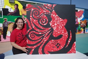 Métis artist Treasure Cooper with her artwork, “Silent Scream” at Kiyam Community Park on May 5, 2023. People at Red Dress Day events were invited to mark the canvas with red paint on their hands. The black lines were covered by tape. The painting shows a woman screaming in pain and anguish while her body is not visible. Cooper said this represents the erasure and invisibility that has surrounded the crisis of missing and murdered Indigenous women, girls and two-spirit people (MMIWG2S). The painting was donated to the Athabasca Tribal Council. Vincent McDermott/Fort McMurray Today/Postmedia Network