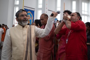 A priest holds up a microphone as Kalpesh Patel blows a conch shell horn called a shankha during Murti Pran Pratishtha, which are the opening ceremonies of a Hindu temple, at the Sanatan Mandir Cultural Society in Fort McMurray on May 22, 2023. The temple is Canada's most northern Hindu temple. Vincent McDermott/Fort McMurray Today/Postmedia Network