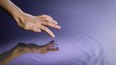 human hand touching the surface of a clear pond of water